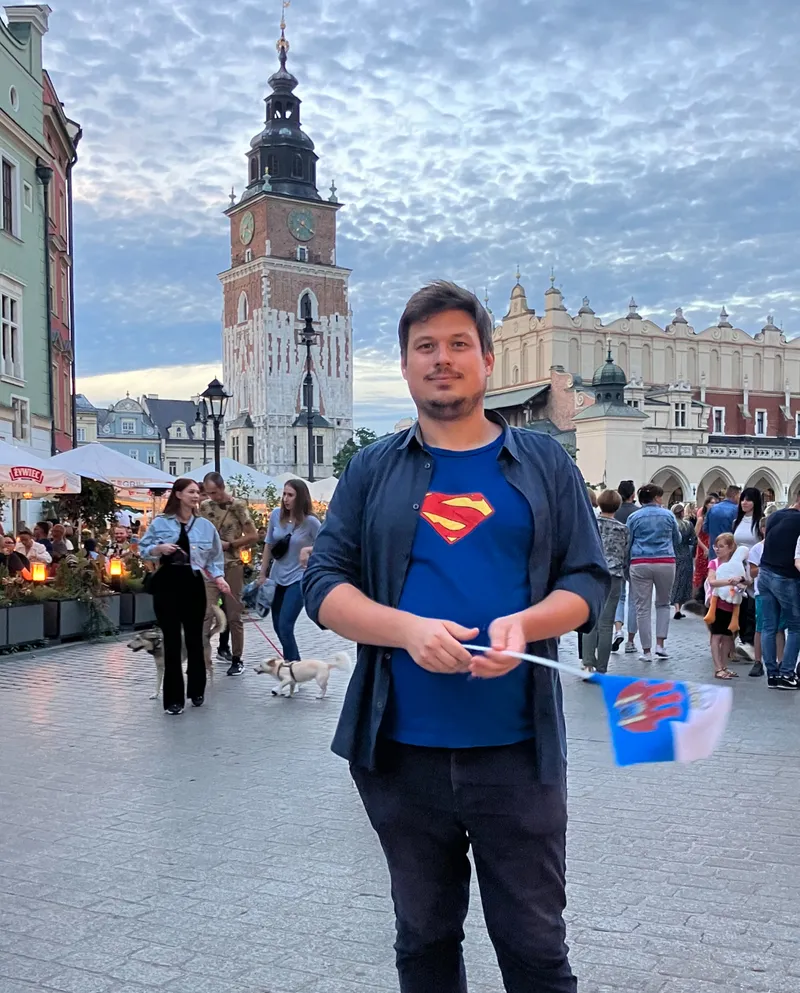 Konrad on the Main Square in front of the Cloth Hall, holding a blue guide umbrella